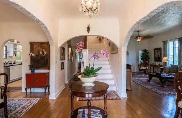 foyer entrance with arched walkways, baseboards, wood finished floors, and ceiling fan with notable chandelier