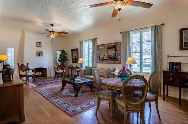 living room featuring a textured ceiling, ceiling fan, a healthy amount of sunlight, and a large fireplace