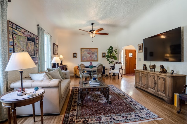 living room with light wood-style floors, arched walkways, a textured ceiling, and a ceiling fan
