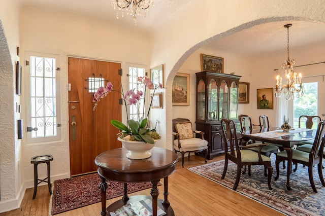 foyer with a healthy amount of sunlight, arched walkways, an inviting chandelier, a textured wall, and light wood-style flooring
