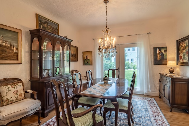 dining space with a textured ceiling, a textured wall, an inviting chandelier, and light wood finished floors