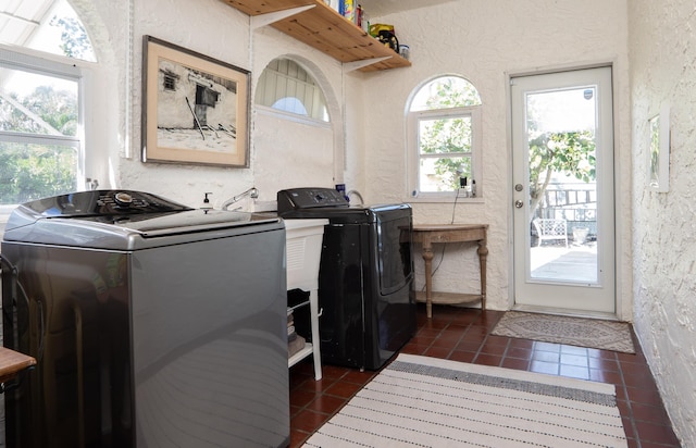 laundry room with dark tile patterned flooring, a textured wall, laundry area, and independent washer and dryer