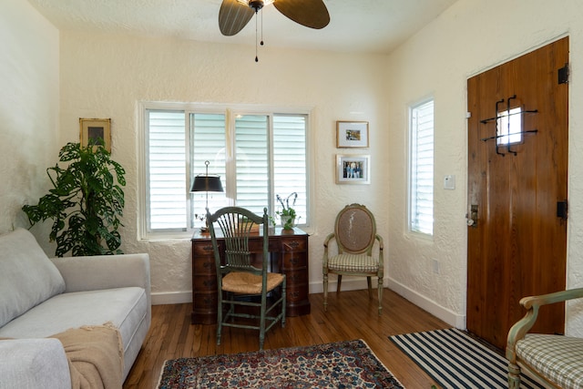 living area featuring baseboards, a textured wall, a ceiling fan, and hardwood / wood-style flooring