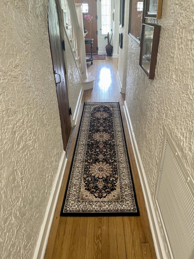 hallway with baseboards, a textured wall, and wood finished floors