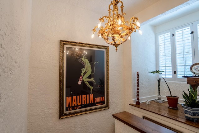 interior space with baseboards, a textured wall, and a notable chandelier