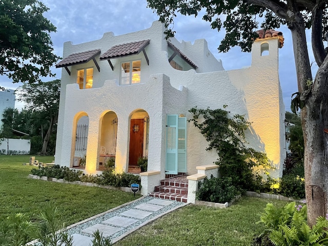 mediterranean / spanish home with fence, a tile roof, a front yard, and stucco siding