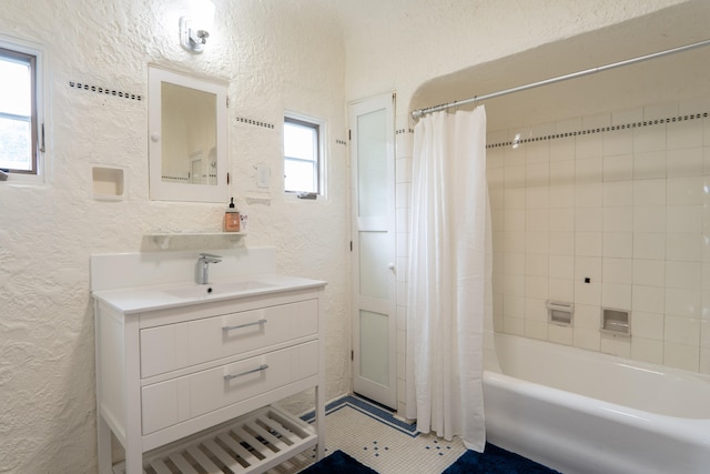 full bath with vanity, a textured wall, and shower / bath combo