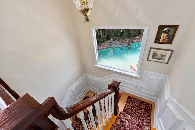 stairway featuring wood finished floors, a decorative wall, a wainscoted wall, and a notable chandelier