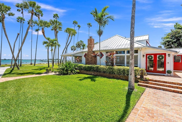 ranch-style house with a front lawn, a chimney, a water view, and metal roof