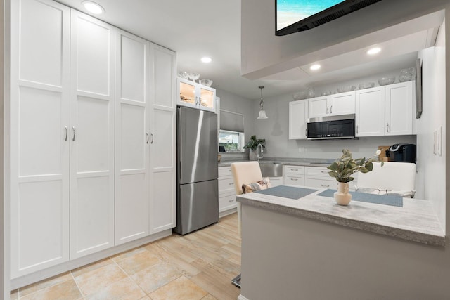 kitchen featuring a sink, white cabinetry, light stone countertops, appliances with stainless steel finishes, and hanging light fixtures