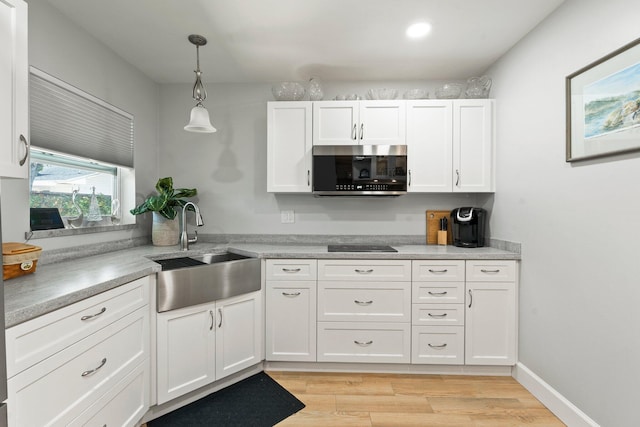 kitchen featuring stainless steel microwave, a sink, white cabinets, and black electric cooktop