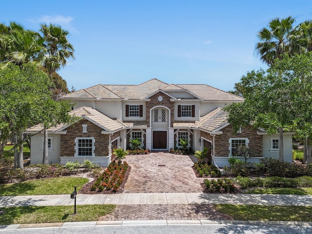 traditional-style house with stone siding, a garage, decorative driveway, and stucco siding