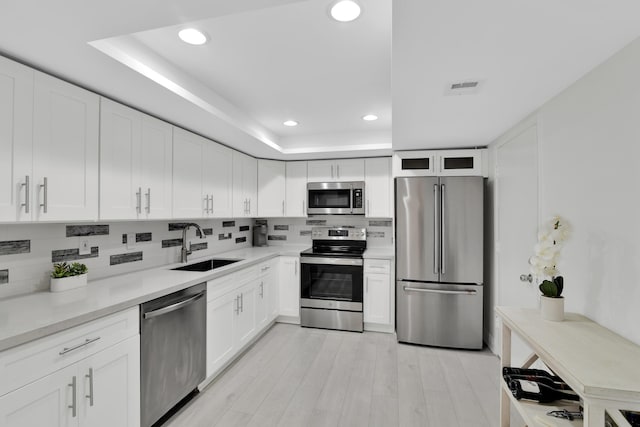 kitchen with a tray ceiling, a sink, tasteful backsplash, recessed lighting, and appliances with stainless steel finishes
