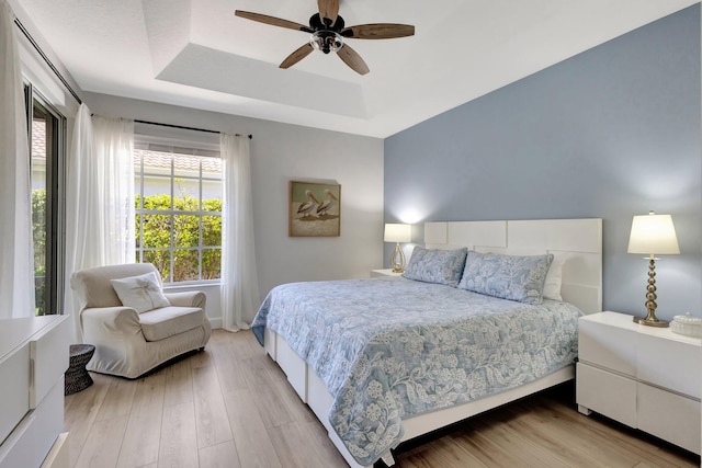bedroom featuring a ceiling fan, light wood-style floors, and a raised ceiling