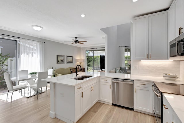 kitchen with light wood finished floors, stainless steel appliances, a ceiling fan, a sink, and a peninsula