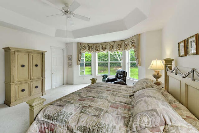 bedroom featuring a ceiling fan, a tray ceiling, and light carpet