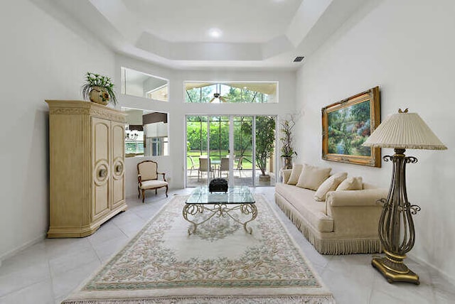 living room with a tray ceiling, baseboards, light tile patterned flooring, a towering ceiling, and a ceiling fan