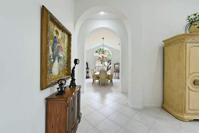 hallway featuring arched walkways, vaulted ceiling, baseboards, a notable chandelier, and light tile patterned flooring