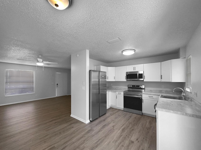 1541 SW Curry St, Port Saint Lucie, FL 34983 - kitchen featuring stainless steel appliances, a textured ceiling, wood finished floors, open floor plan, and white cabinetry