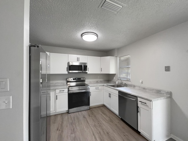 1541 SW Curry St, Port Saint Lucie, FL 34983 - kitchen featuring appliances with stainless steel finishes, a textured ceiling, light wood-type flooring, white cabinetry, and light countertops