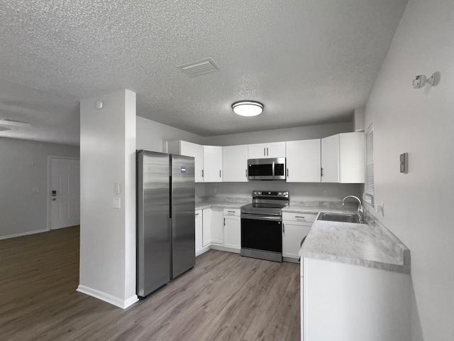 1541 SW Curry St, Port Saint Lucie, FL 34983 - kitchen with appliances with stainless steel finishes, light wood-style flooring, a textured ceiling, light countertops, and white cabinets