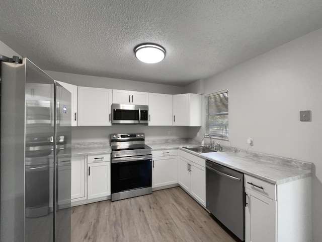 1541 SW Curry St, Port Saint Lucie, FL 34983 - kitchen featuring stainless steel appliances, a textured ceiling, light wood finished floors, white cabinetry, and light countertops