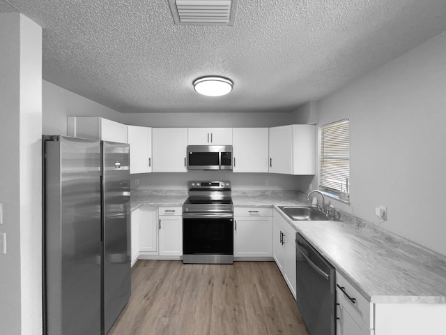 1541 SW Curry St, Port Saint Lucie, FL 34983 - kitchen with appliances with stainless steel finishes, light wood-style flooring, a textured ceiling, light countertops, and white cabinets