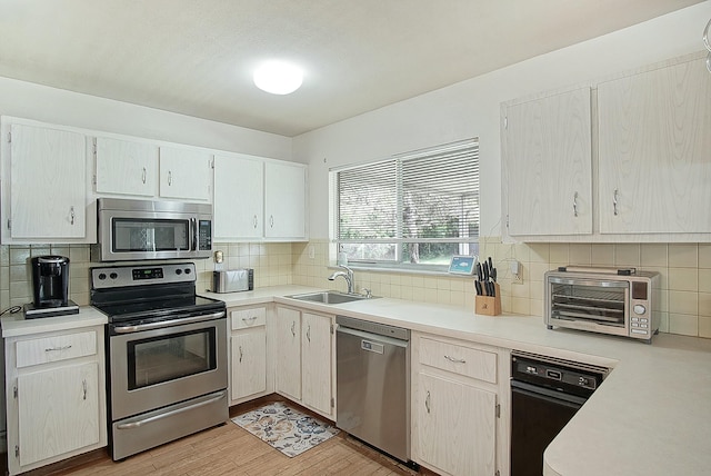 kitchen featuring a sink, decorative backsplash, stainless steel appliances, light wood finished floors, and light countertops