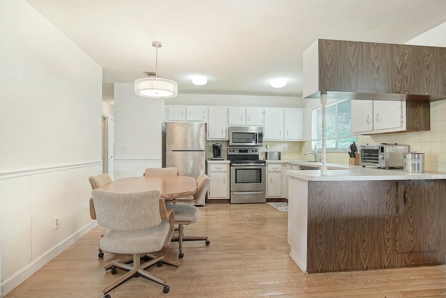 kitchen featuring wainscoting, light wood-type flooring, stainless steel appliances, light countertops, and backsplash