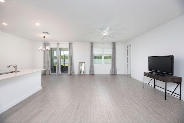 7568 NW Deysbrook Ln, Port Saint Lucie, FL 34987 - unfurnished living room with visible vents, ceiling fan with notable chandelier, a sink, baseboards, and light wood-type flooring