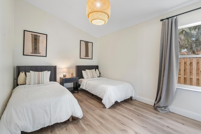 bedroom with lofted ceiling, light wood-style flooring, and baseboards