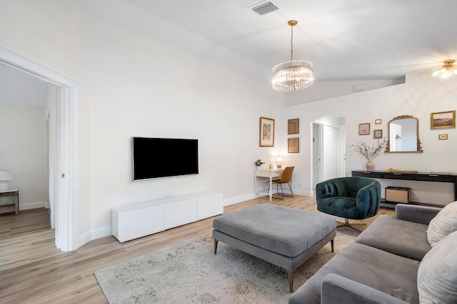 living room featuring light wood-type flooring, an inviting chandelier, visible vents, and arched walkways