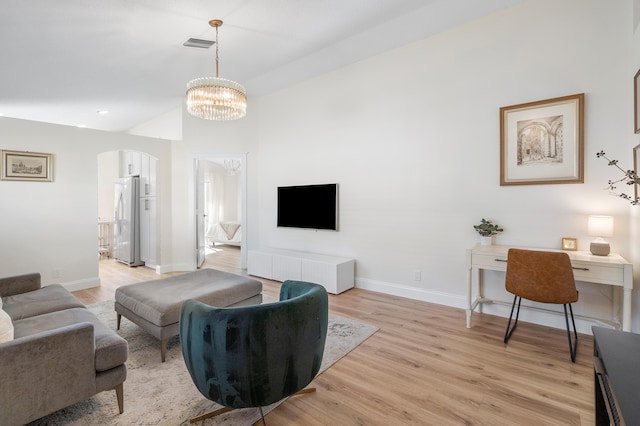 living room with arched walkways, an inviting chandelier, light wood-style flooring, baseboards, and visible vents