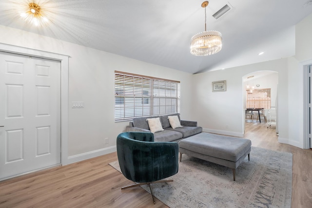 living area with light wood finished floors, vaulted ceiling, visible vents, arched walkways, and a notable chandelier