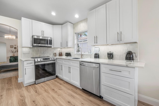 kitchen featuring arched walkways, white cabinetry, stainless steel appliances, and a sink