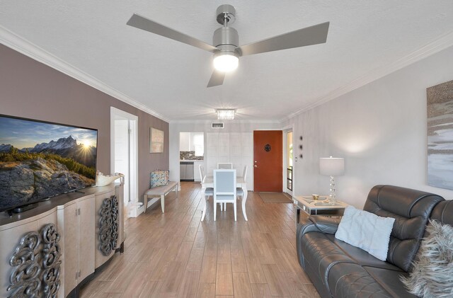 living area with light wood-type flooring, visible vents, a ceiling fan, and ornamental molding