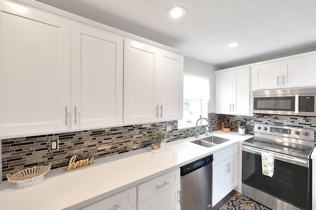kitchen featuring white cabinets, light countertops, a sink, decorative backsplash, and appliances with stainless steel finishes