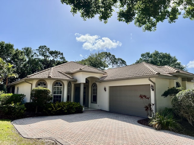 mediterranean / spanish house featuring decorative driveway, an attached garage, a tiled roof, and stucco siding