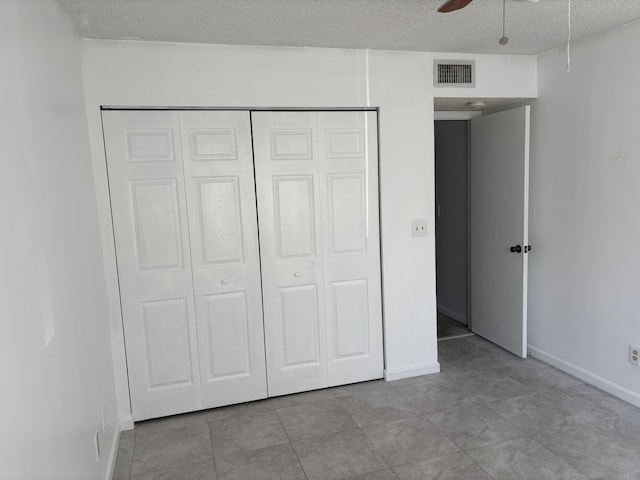 unfurnished bedroom with tile patterned floors, visible vents, a closet, baseboards, and a textured ceiling