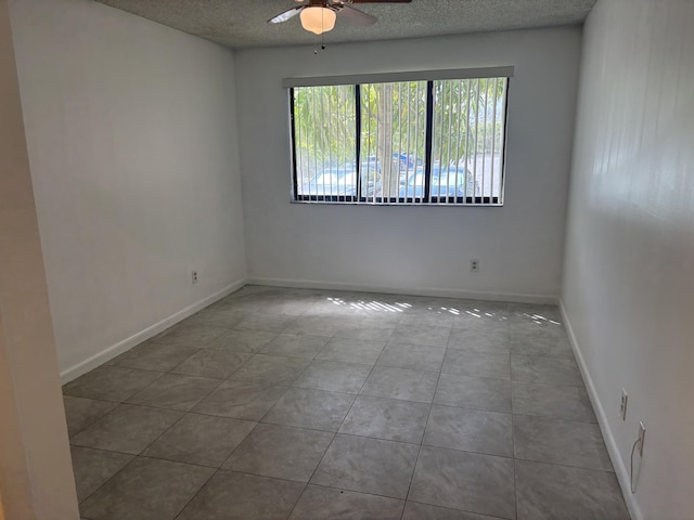 tiled empty room with ceiling fan, baseboards, and a textured ceiling