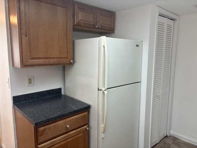 kitchen with freestanding refrigerator, brown cabinetry, visible vents, and tile patterned floors