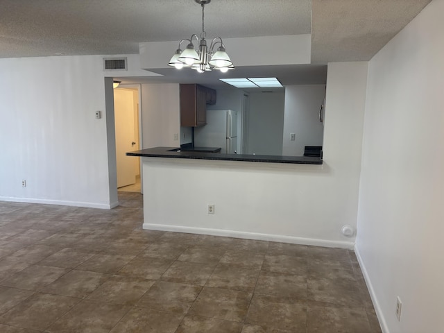 kitchen featuring dark countertops, a chandelier, baseboards, visible vents, and freestanding refrigerator