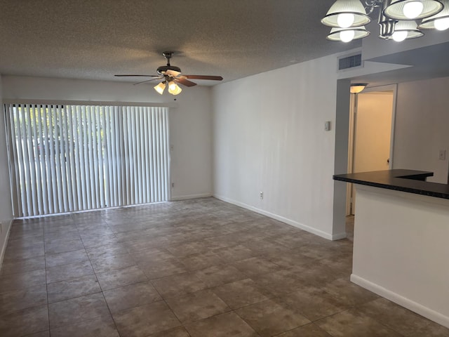 unfurnished living room with a textured ceiling, visible vents, baseboards, and ceiling fan with notable chandelier