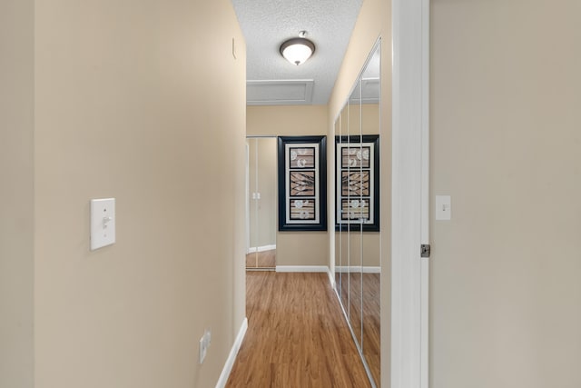 corridor featuring baseboards, wood finished floors, and a textured ceiling
