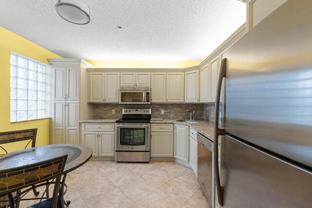 kitchen with light tile patterned floors, a sink, decorative backsplash, a textured ceiling, and appliances with stainless steel finishes