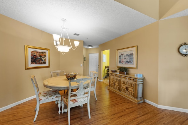 dining space with wood finished floors, visible vents, baseboards, and a notable chandelier