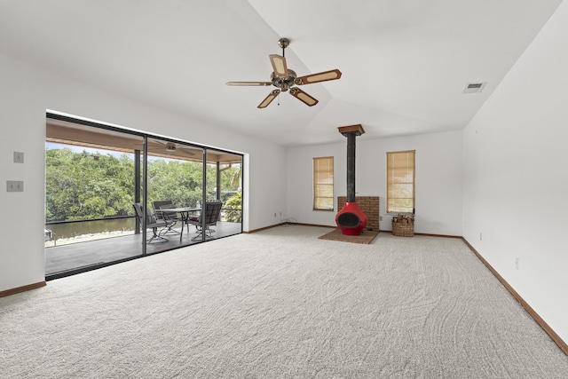 carpeted spare room featuring visible vents, a wood stove, lofted ceiling, baseboards, and ceiling fan