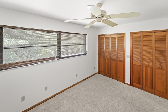 unfurnished bedroom with carpet floors, a ceiling fan, baseboards, and multiple closets