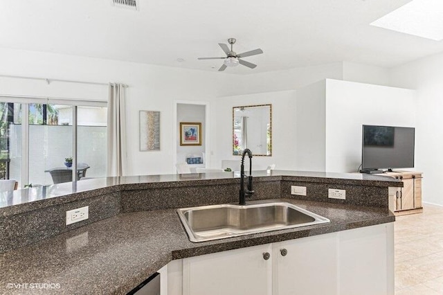 kitchen featuring dark countertops, open floor plan, ceiling fan, white cabinetry, and a sink