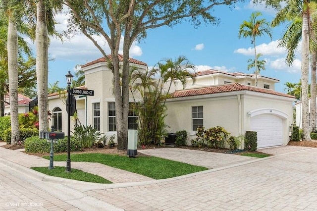 mediterranean / spanish-style home with a garage, stucco siding, a tiled roof, and decorative driveway